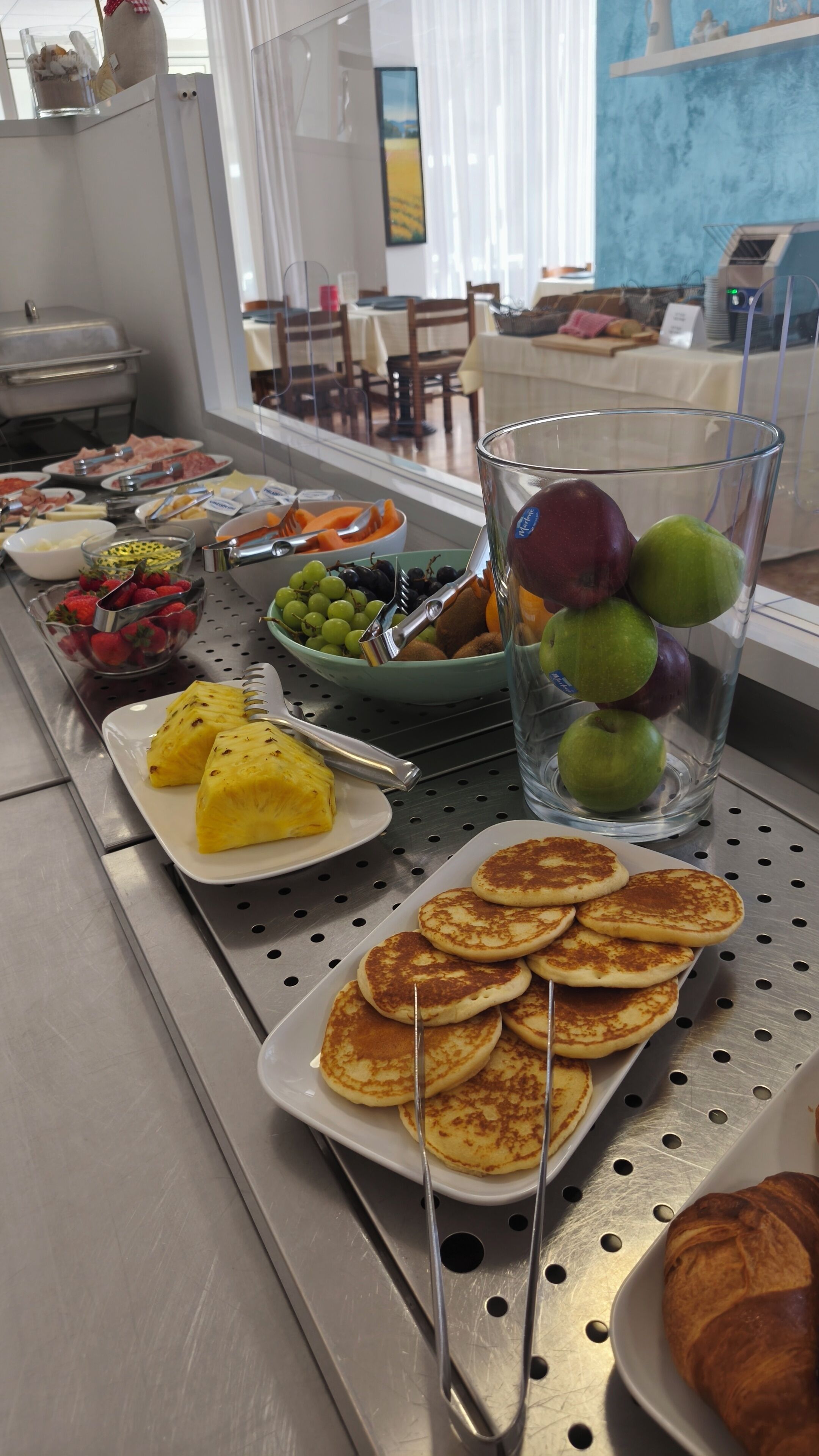 A buffet with various food items including fruits, vegetables, and pancakes.
