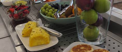 A buffet with various food items including fruits, vegetables, and pancakes.