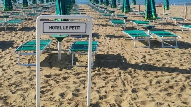 A beach with rows of green umbrellas and lounge chairs, a sign reading "HOTEL LE PETIT". - Le Petit Hotel (Lido di Jesolo)