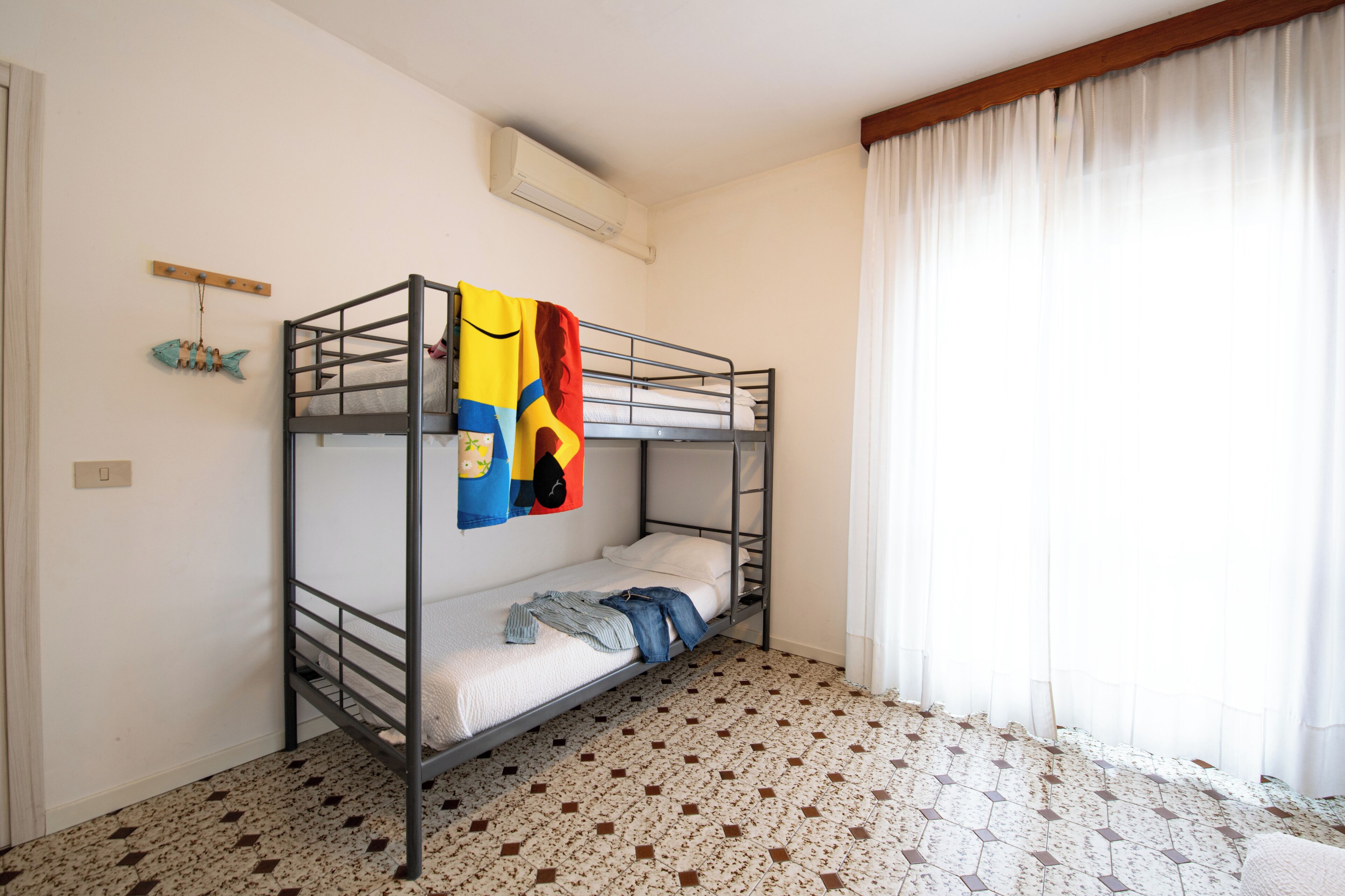 A bunk bed room with a tiled floor, a window with curtains, and a wall-mounted air conditioner.