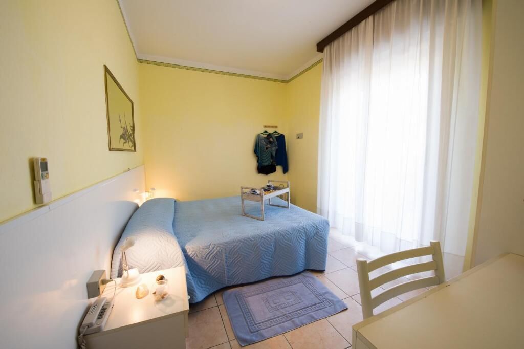 A small, well-lit bedroom with a bed, bedside table, and a chair.