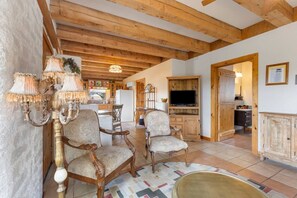 A rustic interior with wooden beams, antique chairs, a television, and a kitchen area. - Adobe Vista - Cozy and inviting, spectacular view! (Alpine)