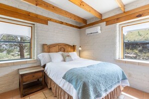 A bedroom with a wooden headboard, a bed with white bedding and a blue blanket, a nightstand, and a window with an air conditioning unit. - Adobe Vista - Cozy and inviting, spectacular view! (Alpine)