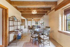 Un coin repas avec une table ronde et des chaises, des poutres en bois au plafond et une fenêtre avec des stores.