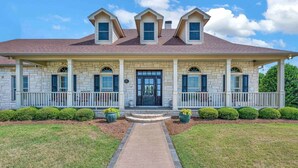 A two-story house with a stone facade, a front porch with white railings, and a central entrance. - The Green Ranch House-Pool-Theatre-Hot Tub-Game Ro (Lorena)