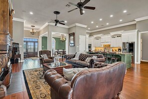 A spacious living room with a fireplace, leather sofas, a coffee table, and a dining area with a chandelier.