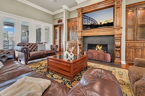 A spacious living room with leather sofas, a glass coffee table, and a fireplace with a stone facade.