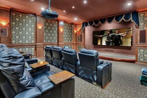 A home theater with leather reclining seats, a large flat-screen TV, and patterned wallpaper.