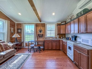A kitchen with wooden cabinets, a stove, and a dining area with a table and chairs. - Wagon Wheel Cottage Couples Getaway in the Country (Waco)