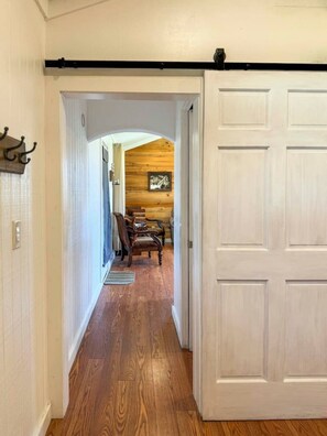 A hallway with wooden flooring, a white door, and a rustic wall with a framed picture. - Wagon Wheel Cottage Couples Getaway in the Country (Waco)