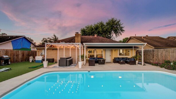 A backyard with a swimming pool, a covered patio with outdoor furniture, and a wooden fence. - Your Houston Vacation Getaway, 4-BD, Pool, Patio (Houston)