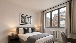 A modern hotel room with a large bed, two bedside tables, a desk, and a window with a view of buildings. - Spacious & Quiet AC 2 Bed By Liverpool St/Spitalfields (London)