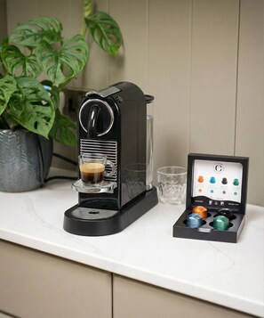 Una máquina de café con jarra de vidrio y un portacápsulas con varias cápsulas.
