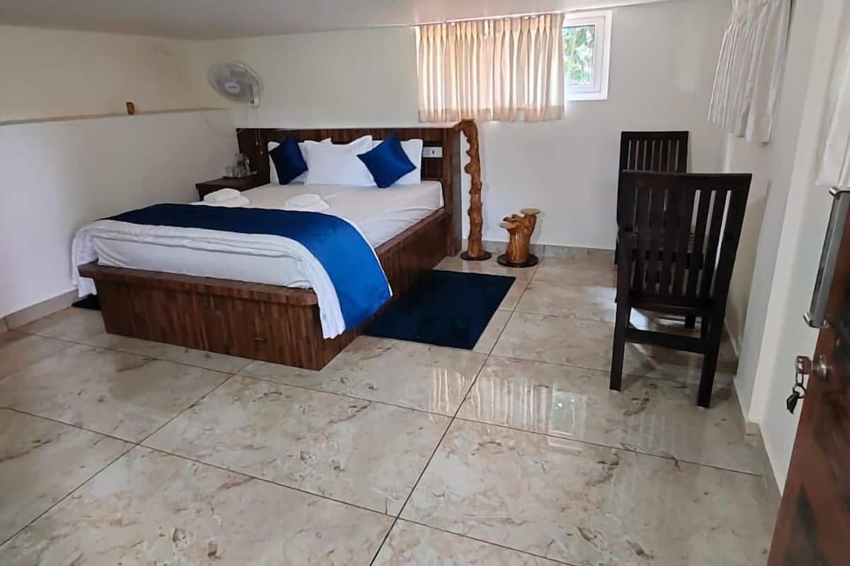 A bedroom with a bed, a chair, a fan, and a window with curtains.