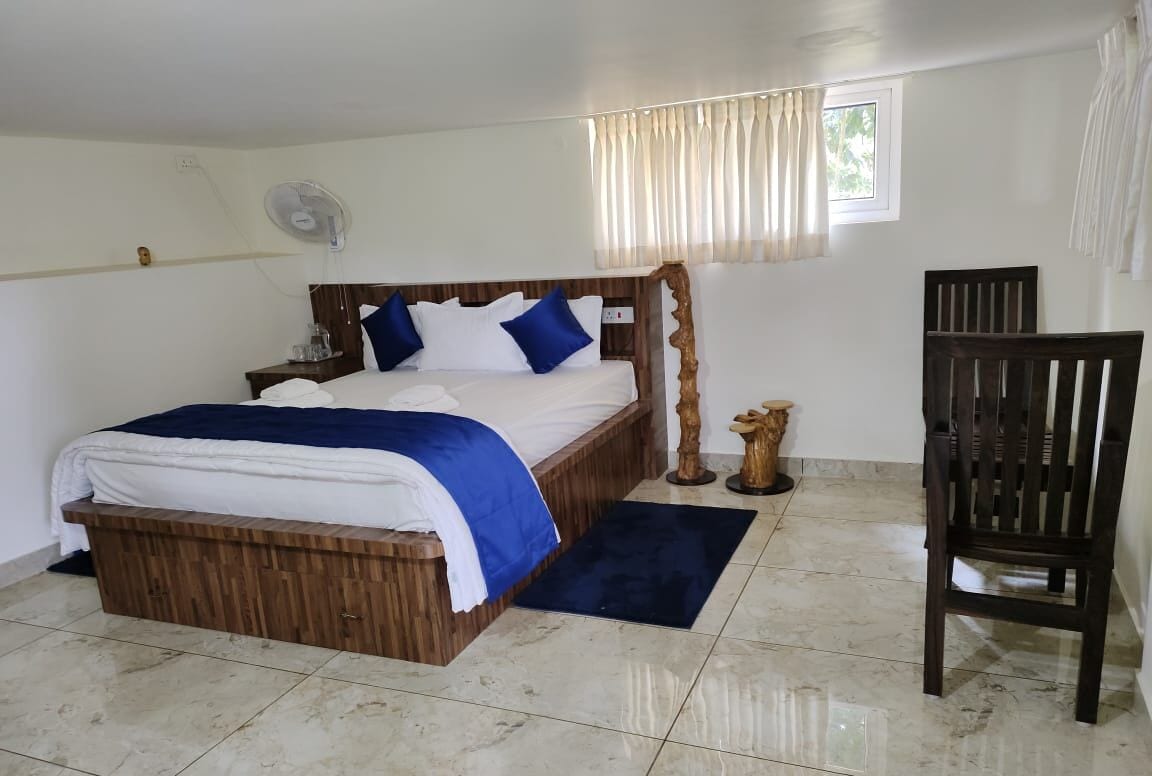 A bedroom with a wooden bed, a bedside table, a chair, and a small wooden sculpture.