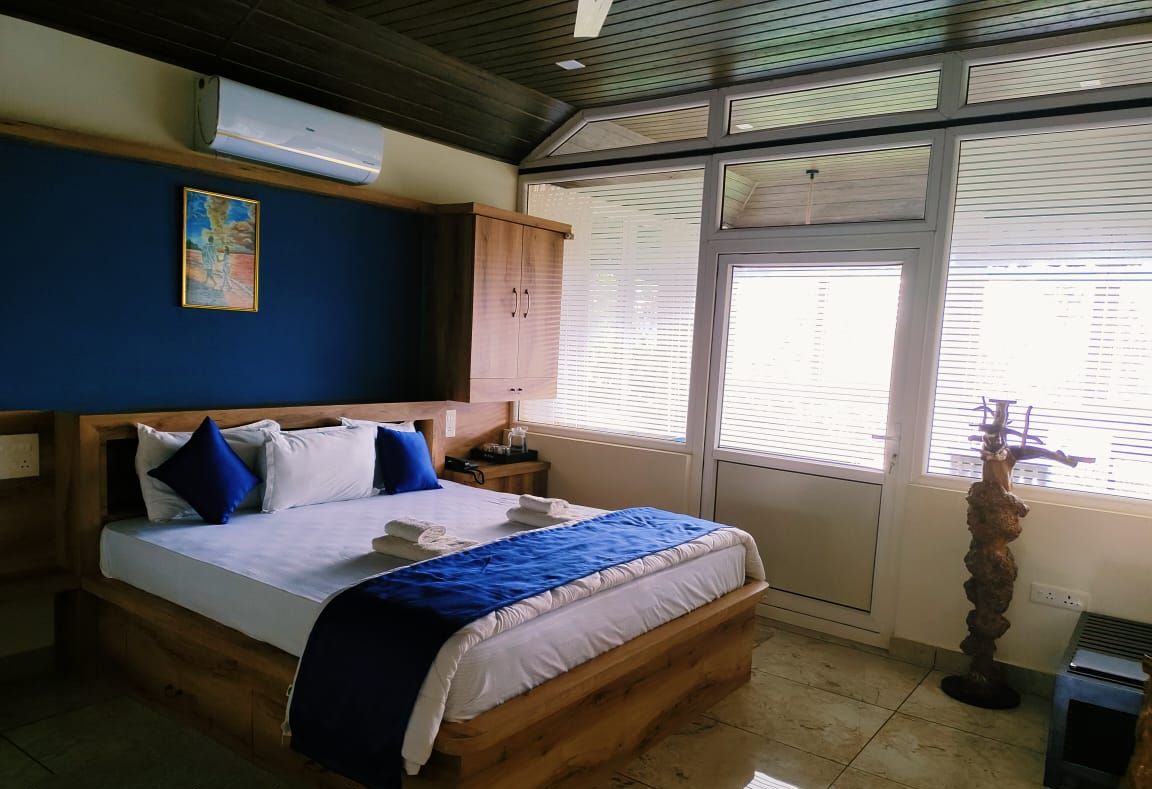Un dormitorio con una cama de madera, una pared azul, una ventana con persianas y una estatua.
