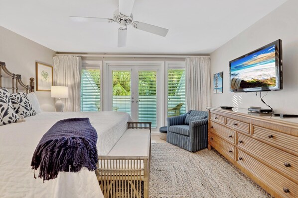 A bedroom with a bed, a TV, a dresser, a chair, and a view of the outdoors.