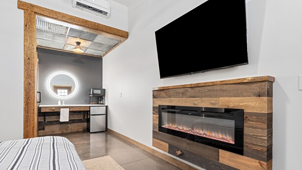 Een moderne slaapkamer met een groot bed, een open haard, een televisie en een kitchenette.