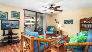 Ein Wohnzimmer mit Fernseher, blauen Sofas, einem Holztisch und einem Deckenventilator.