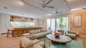 A modern living room with a sofa, chairs, a coffee table, and a kitchen area with a dining table and chairs. - The Rigby House - Pool, One block from Duval St (Key West)