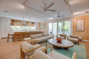 Uma sala de estar moderna com sofá, cadeiras, mesa de centro e área de cozinha com mesa de jantar e cadeiras.