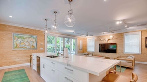 A modern kitchen with a large island, pendant lights, and a television on the wall. - The Rigby House - Pool, One block from Duval St (Key West)