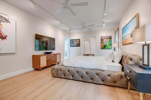 A bedroom with a tufted bed, a wooden dresser, a ceiling fan, and artwork on the walls. - The Rigby House - Pool, One block from Duval St (Key West)