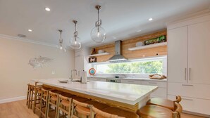 A modern kitchen with a central island, bar stools, pendant lights, and a view of greenery outside. - The Rigby House - Pool, One block from Duval St (Key West)