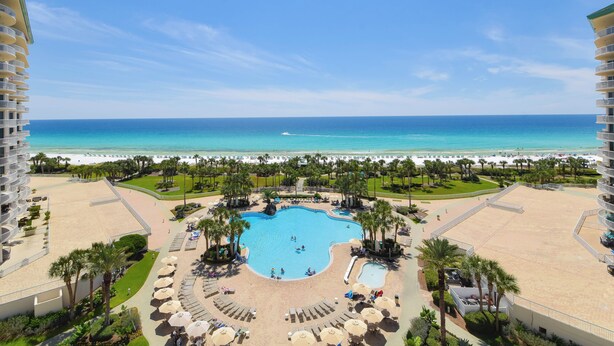 A resort with a central swimming pool surrounded by palm trees and lounge chairs, overlooking a beach and ocean. - Serene Beachfront Condo w/ Beach Service in Central Destin! 🌴🐚🌊 (Destin)