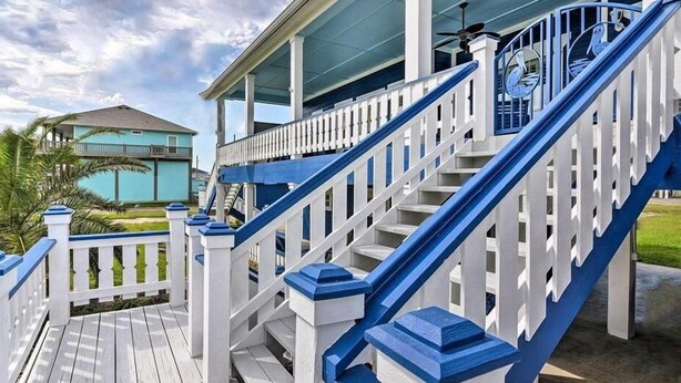 A wooden deck with white railings and blue accents, leading to a covered porch area. - Yoho Hideout 4 Bedroom Home by RedAwning (Port Bolivar)
