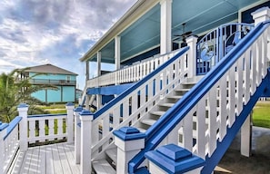 Una terraza de madera con barandillas blancas y detalles azules, que conduce a un porche cubierto.