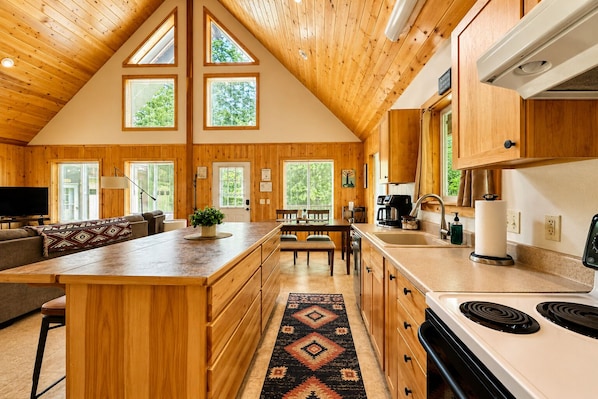 A spacious kitchen with wooden cabinetry, a central island, and a dining area with a view of the outdoors. - Pine River Retreat 2 Bedroom Home by RedAwning (Leavenworth)