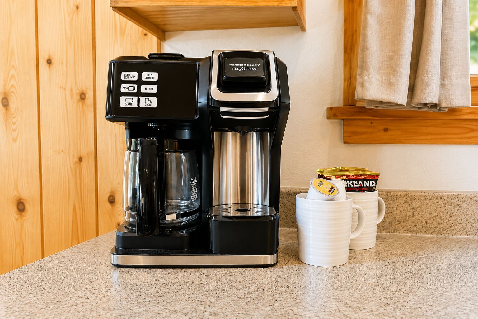 A coffee maker with a digital display, a carafe, and a mug on a countertop.