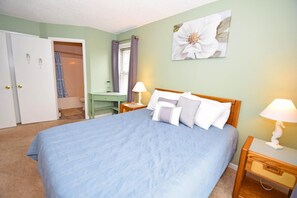A bedroom with a large bed, a desk, a chair, and a wall-mounted lamp. - Sunset Landing 24 2 Bedroom Townhouse by RedAwning (Ocean City)