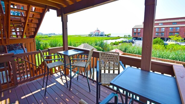 A wooden deck with a table and chairs, overlooking a green field and buildings. - Sunset Landing 24 2 Bedroom Townhouse by RedAwning (Ocean City)