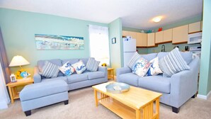 A living room with two sofas, a coffee table, and a kitchen area in the background. - Sunset Landing 24 2 Bedroom Townhouse by RedAwning (Ocean City)