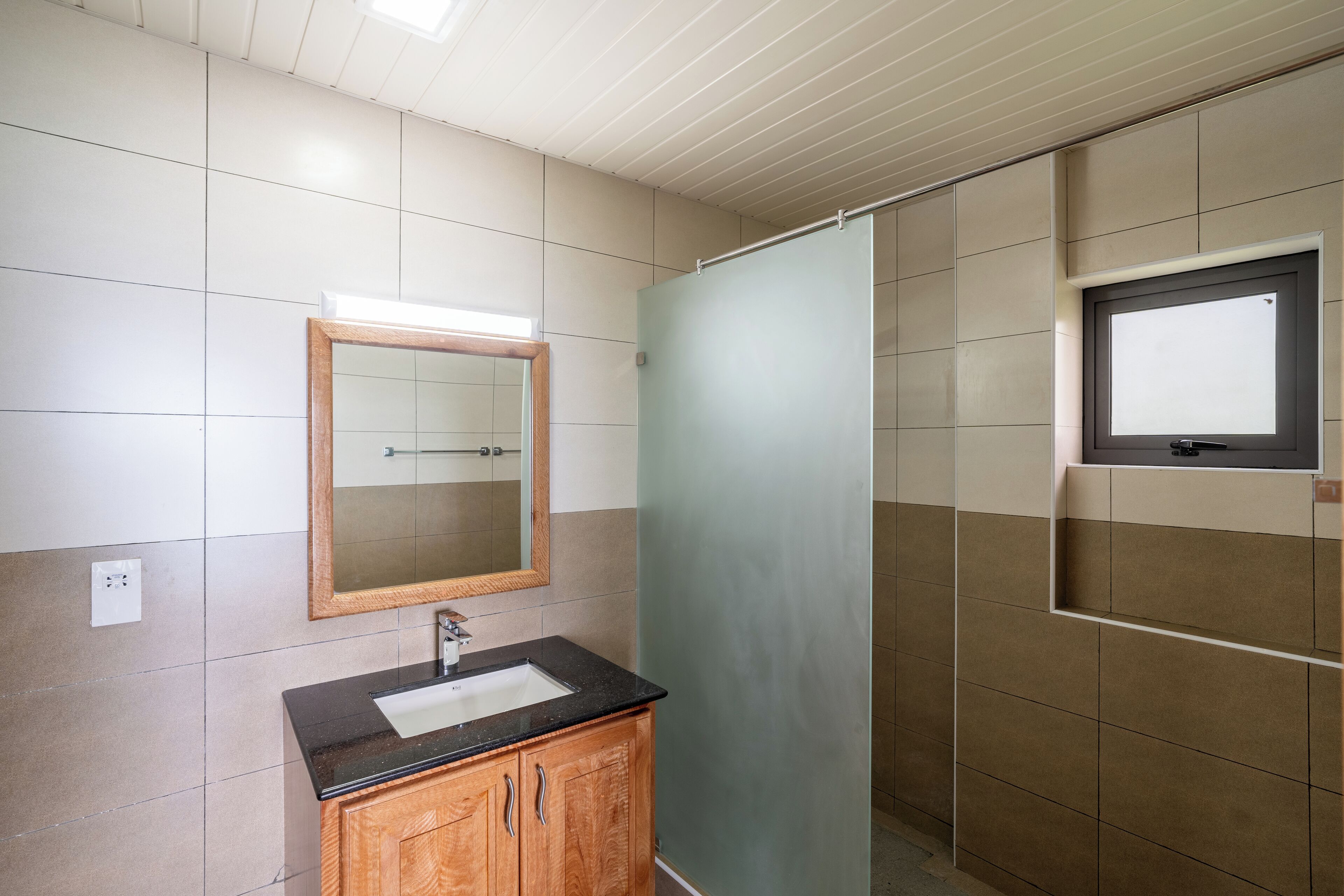 A bathroom with a wooden cabinet, a mirror, and a shower area.