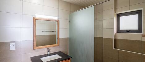 A bathroom with a wooden cabinet, a mirror, and a shower area.