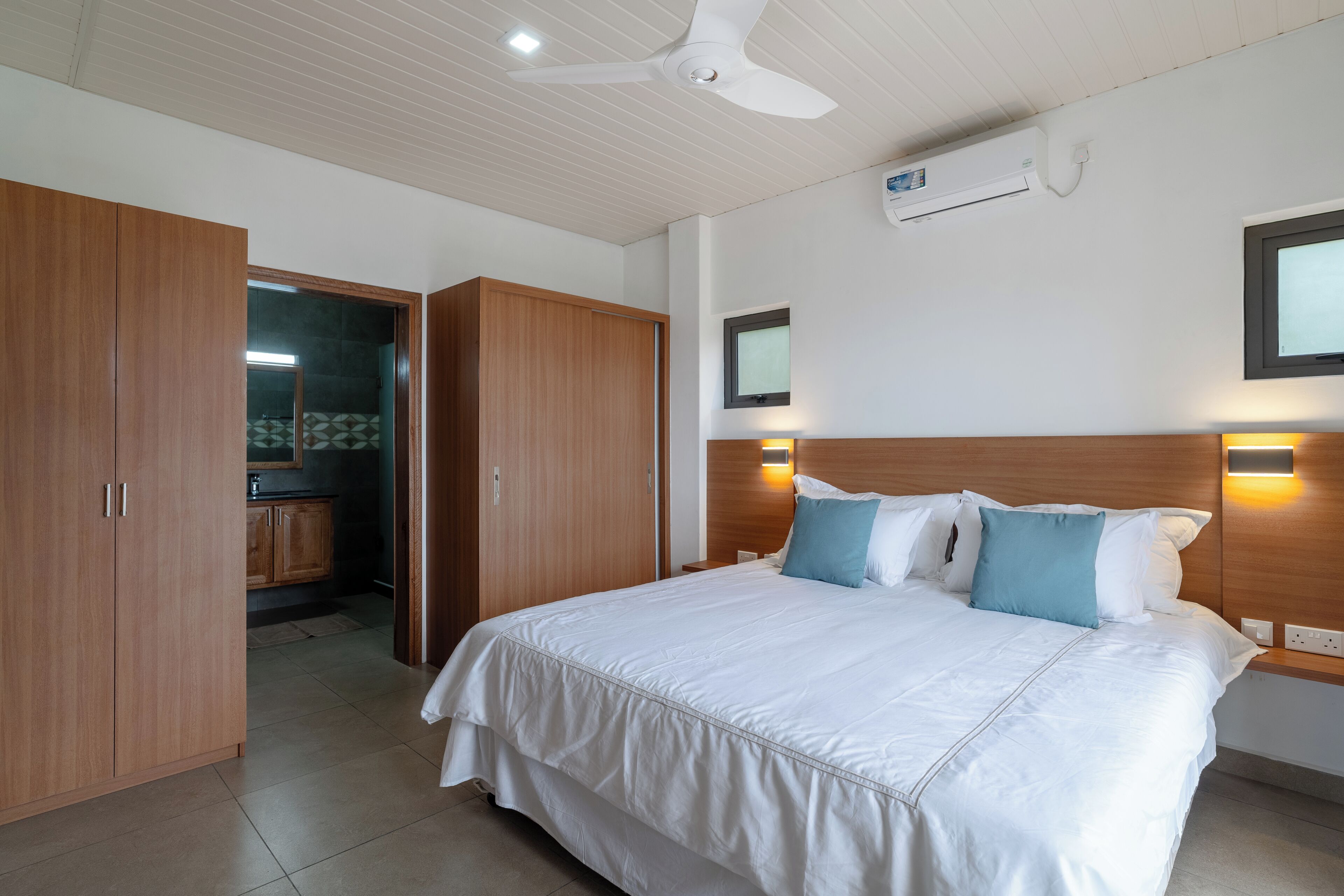 A bedroom with a large bed, wooden wardrobe, and a ceiling fan.