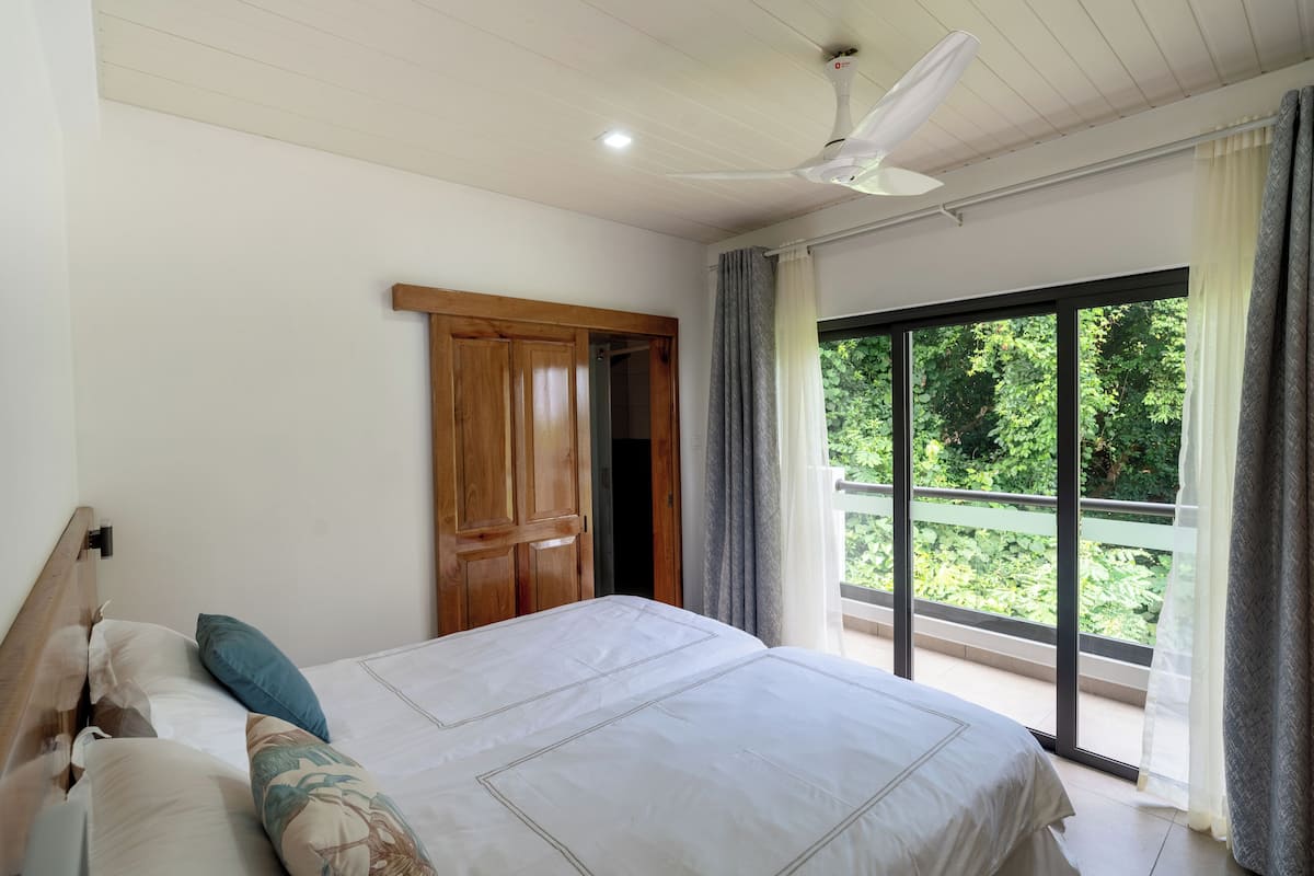A bedroom with a large bed, wooden wardrobe, and a balcony with a view of greenery.