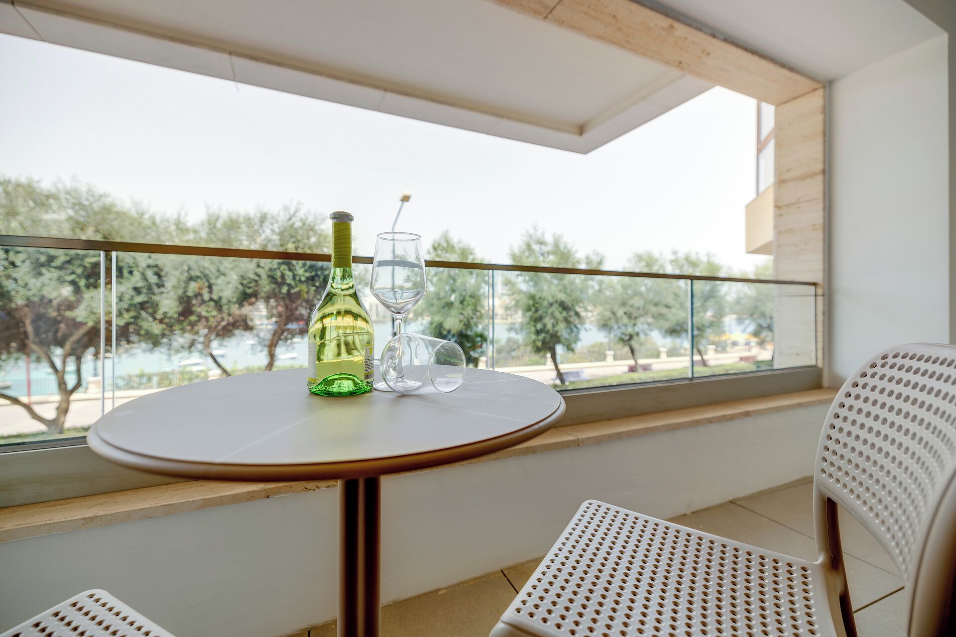 A balcony with a round table, a bottle of white wine, and two glasses.