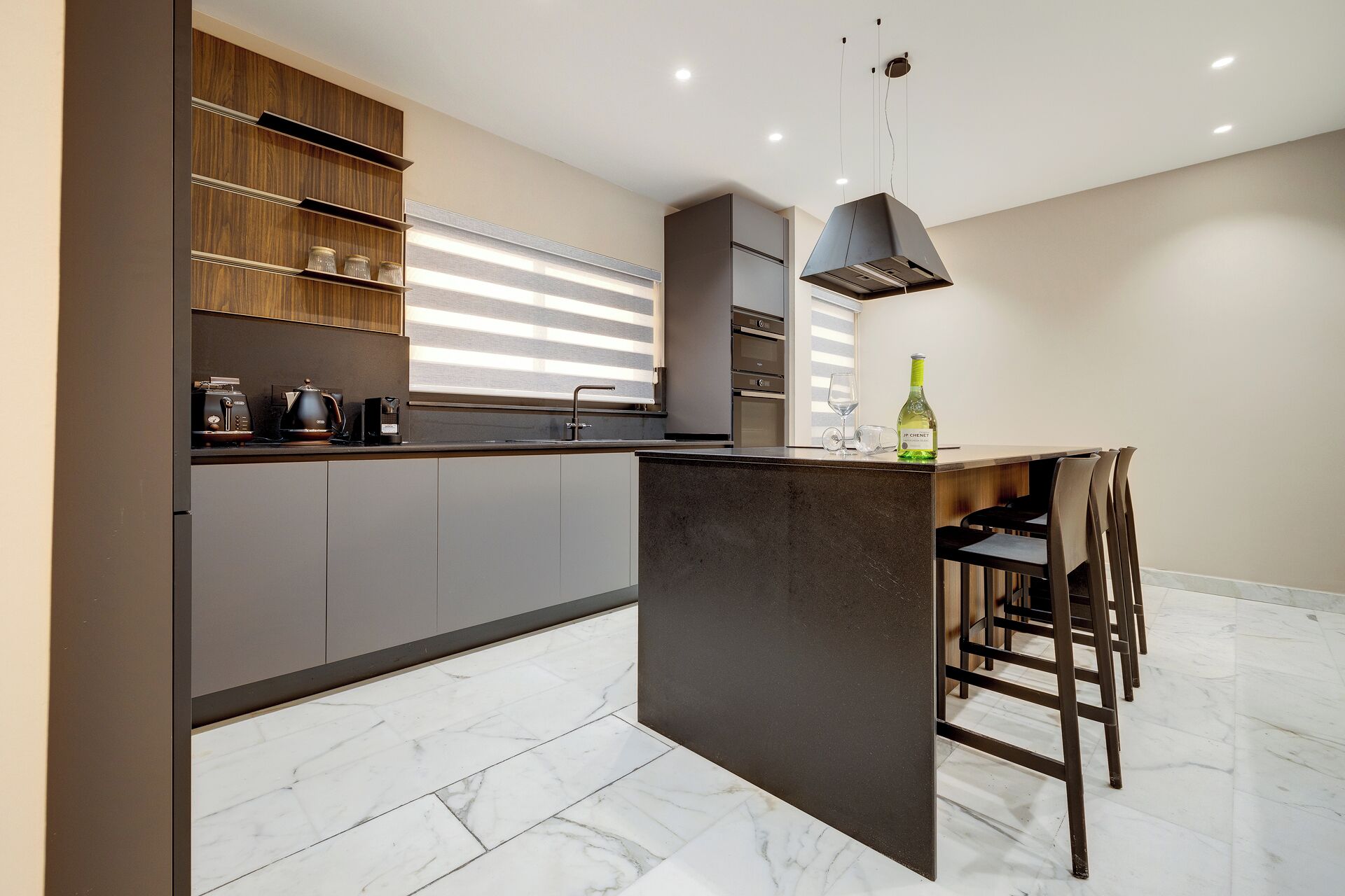 Een moderne keuken met een centraal eiland, inbouwapparatuur en een eethoek met stoelen.
