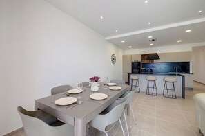 A modern kitchen with a central island, bar stools, and a dining area with a table set for four. - Elegant Sliema Penthouse, Panoramic Terrace (Sliema)
