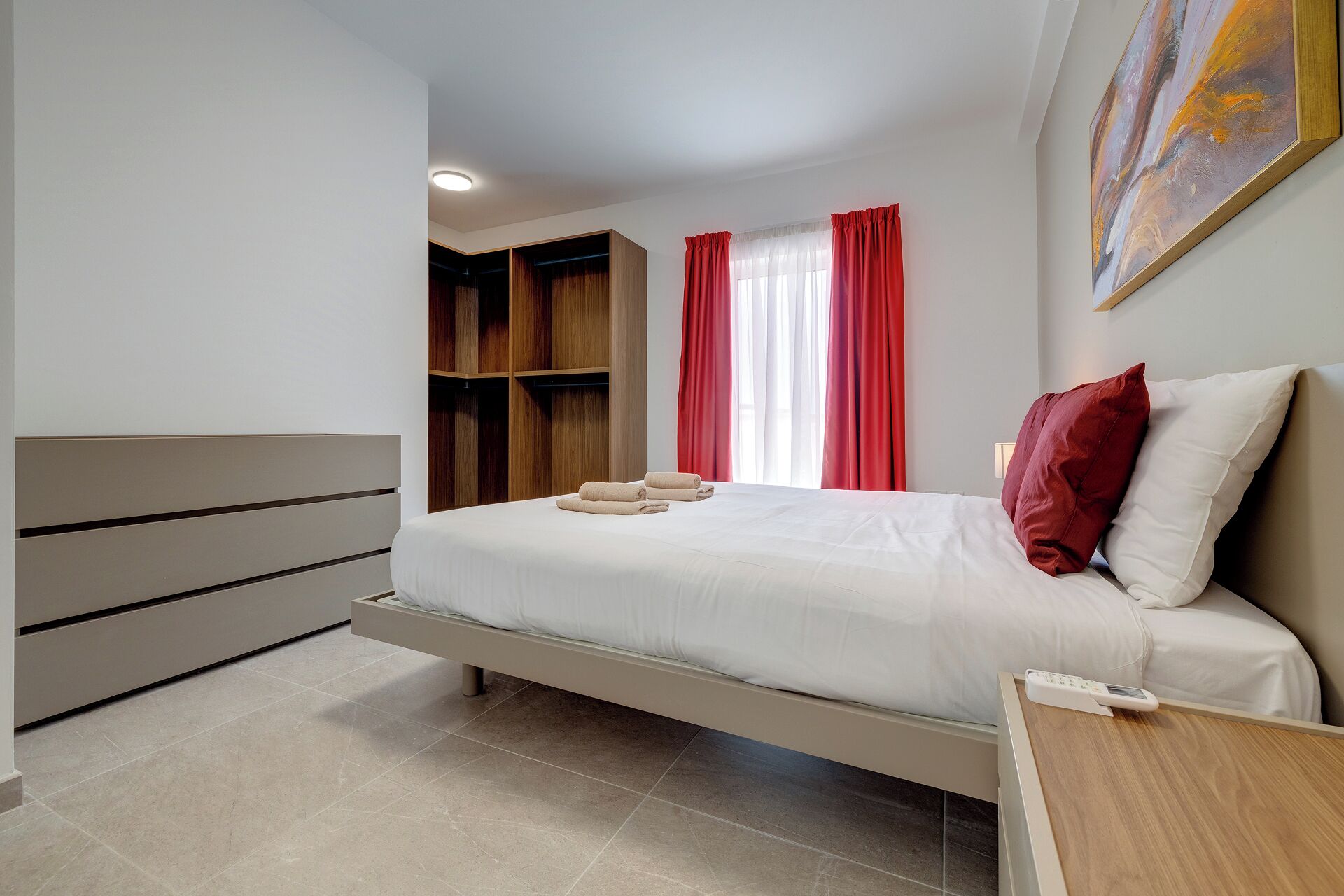 A modern bedroom with a bed, a wooden wardrobe, a bedside table, and a painting on the wall.