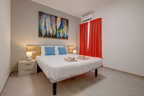 A neatly arranged hotel room with a large bed, two bedside tables with lamps, a painting above the bed, and a red curtain. - Elegant Sliema Penthouse, Panoramic Terrace (Sliema)