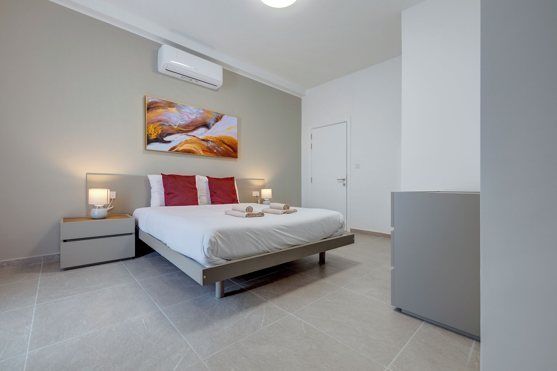 Een moderne slaapkamer met een bed, nachtkastjes, een schilderij en een airconditioner.