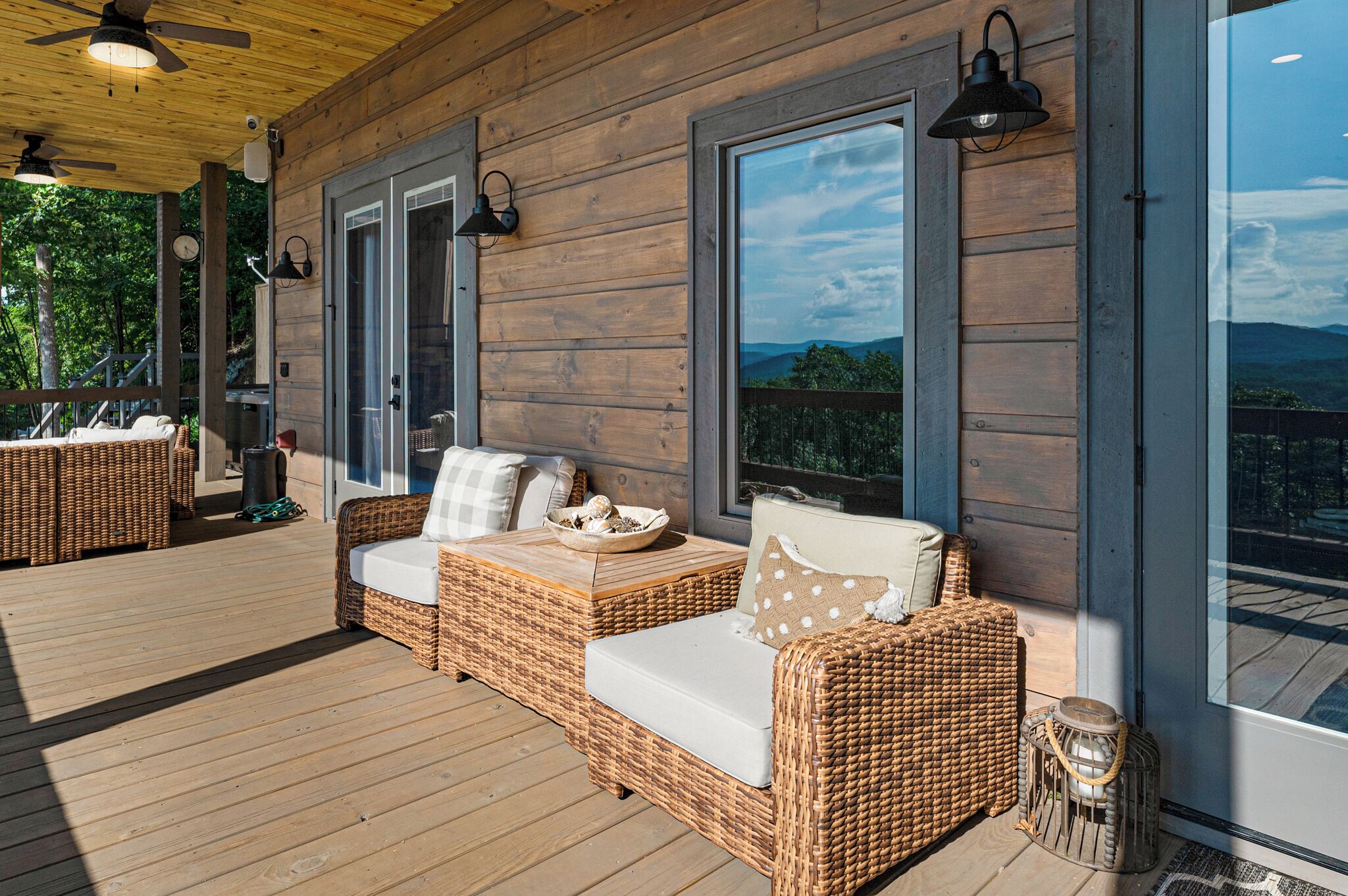 A wooden deck with wicker furniture and large windows offering a view of the outdoors.