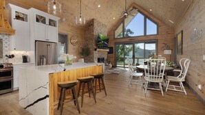 A spacious kitchen with a large island, wooden cabinets, and a stone accent wall. - Elevated Escape Blue Ridge GA (Blue Ridge)