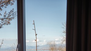 A room with a large window overlooking a terrace with a view of mountains and a body of water. - Hotel Flaer (Shkodër)
