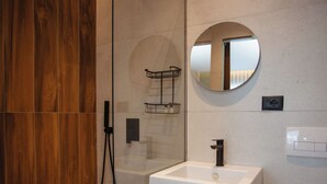 A modern bathroom with a glass-enclosed shower, a white sink, and a round mirror. - Hotel Flaer (Shkodër)